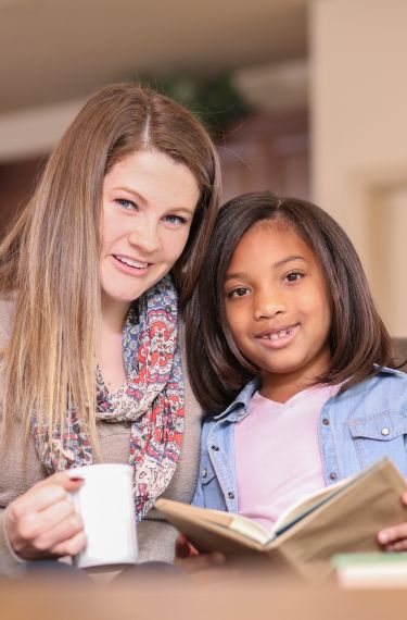 smiling woman holding cup and young girl holding book