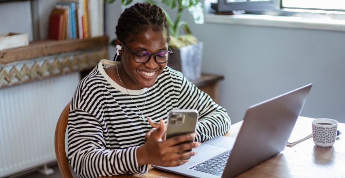 Woman looking at cellphone while sitting in front of laptop