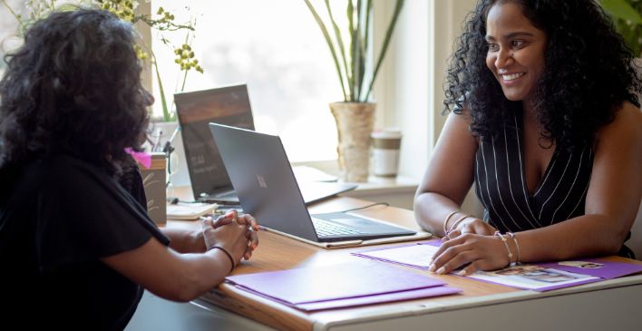 Two women sitting across from a desk talking to each other