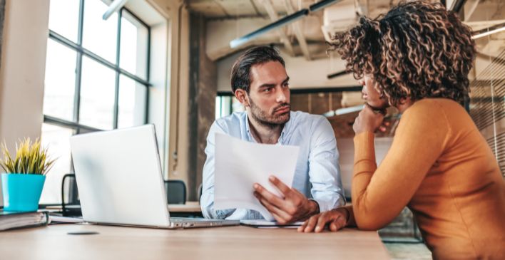 Man holding a piece of paper talking to a woman at a table