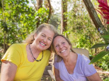 Two smiling middle-aged women with their heads tilted toward each other 