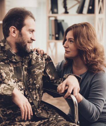 Military servicemember in a wheelchair with his wife next to him holding his hand