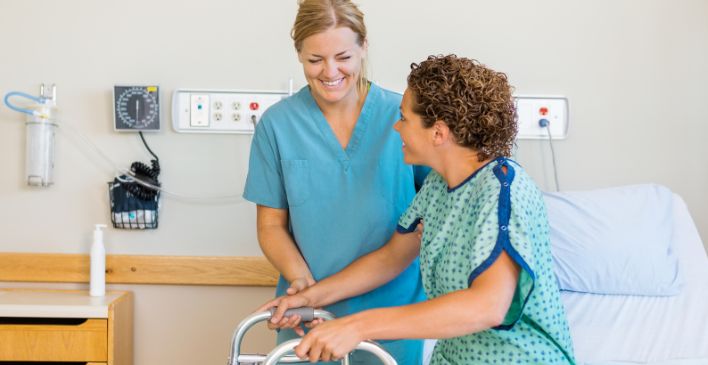 Woman in hospital gown with a walker being assisted by a nurse