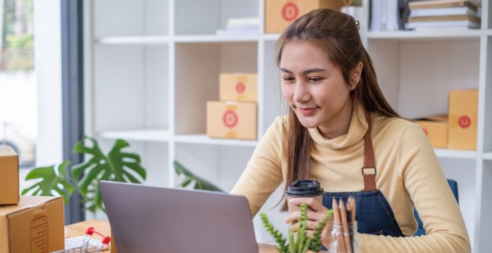 Woman in apron holding coffee looking at a laptop